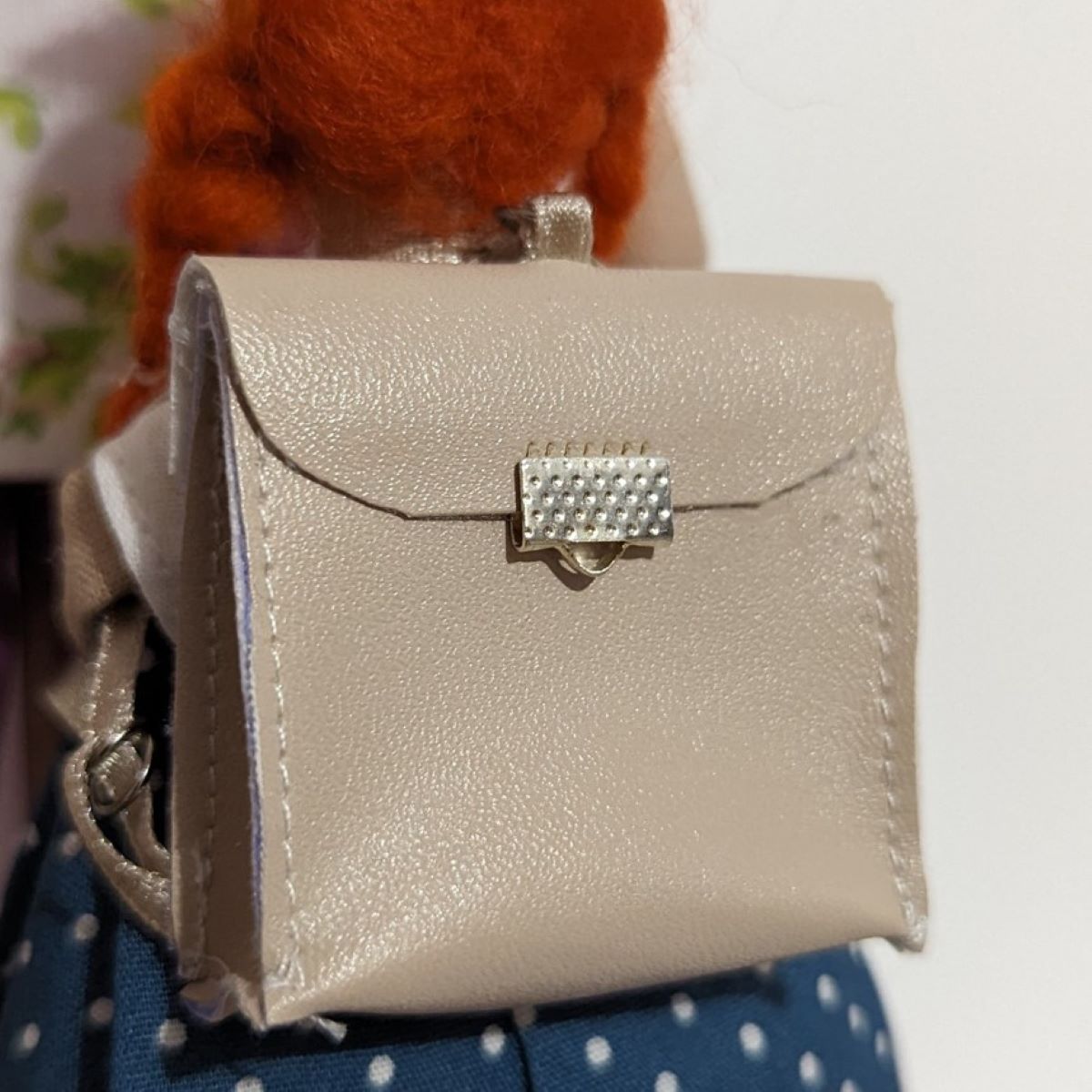 Détail du cartable de la poupée: simili taupe, fermoir, et couture apparente.