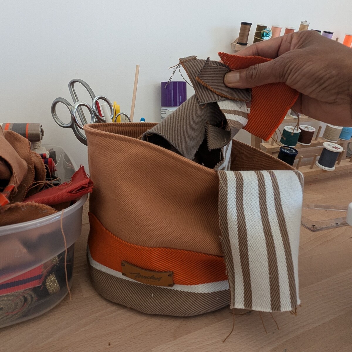 Une main tenant des chutes de tissu au dessus d'une panière en toile basque aux tons orangé posé sur une table