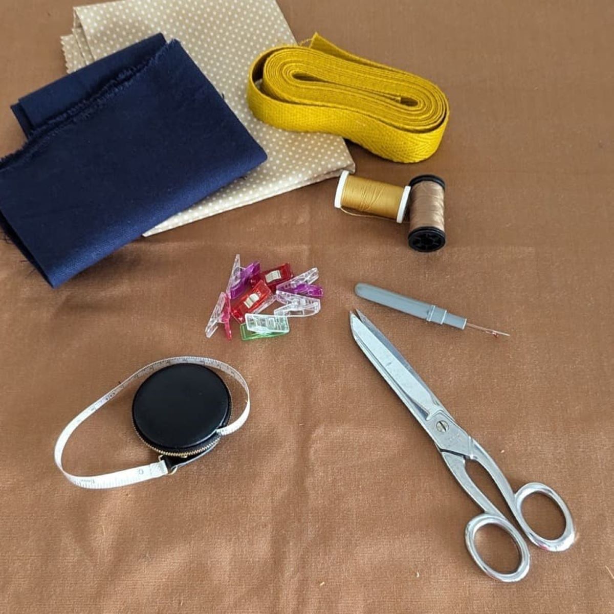 Matériel de couture posé sur une table : mètre ruban, ciseaux pinces, fil , tissus.