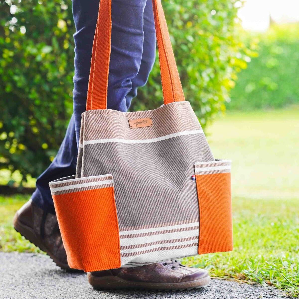 Le sac en chutes de toile basque orange et taupe porté à la main par les grandes anses